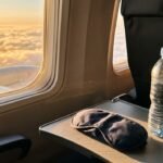 Airplane window at sunrise with a sleeping mask and water bottle, illustrating jet lag and light exposure during long-haul travel
