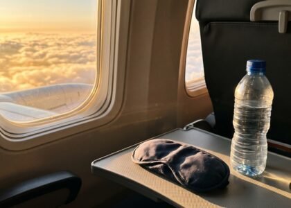 Airplane window at sunrise with a sleeping mask and water bottle, illustrating jet lag and light exposure during long-haul travel